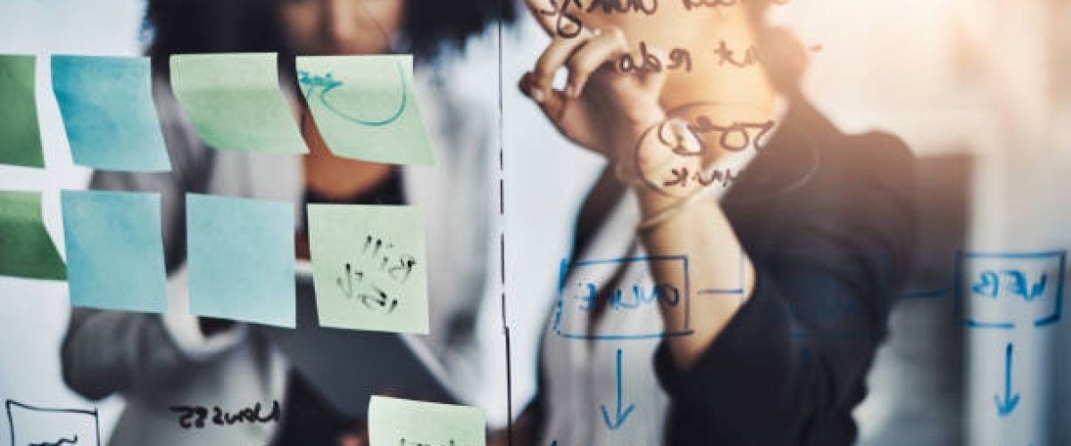 Shot of two businesswomen brainstorming with notes on a glass wall in an office