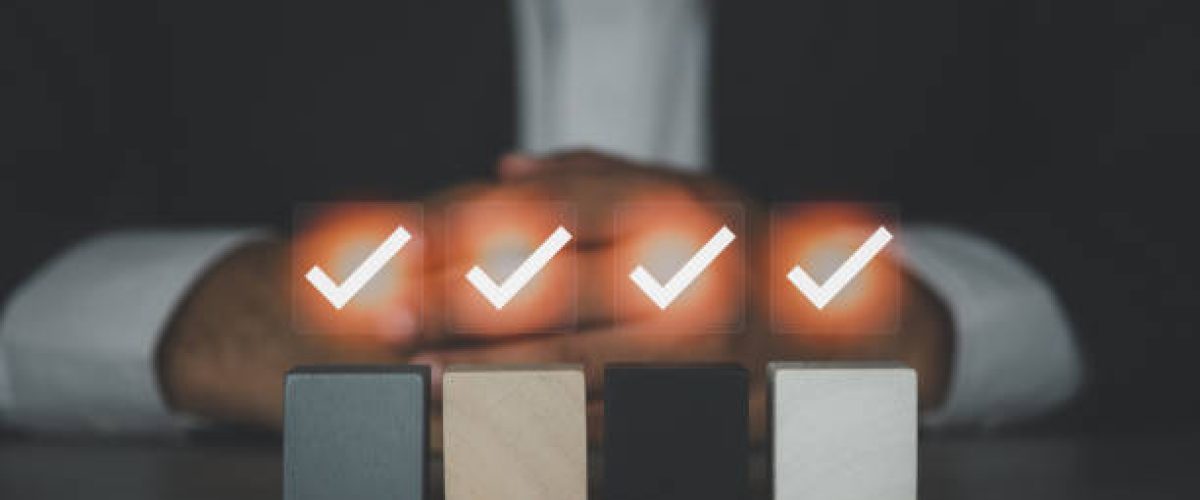 a businessman with clasped hands behind check mark on an empty wood block. Checklist or to do list in business concept